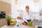 Smart girl slices cucumber with knife and smiles, standing at ki