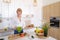 Smart girl slices cucumber with knife and smiles, standing at ki