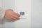 Smart home concept. Hands puches button switch on white wall, regulates temperature in flat or room. Close up, selective focus.