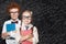 Smart kids portrait. Little girl and boy student holding books and standing against blackboard background with science and maths