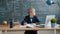 Smart little boy writing at desk in class, formulas are on chalkboard in background