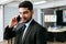 Smart and positive businessman calling and talking on smart phone alone in the office. Professional making business calls.