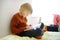 Smart preteen boy sitting on bed and enthusiastically reading interesting book. Kid reader enjoying interesting stories, reading