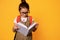 Smart primary school student girl in eyeglasses, carrying backpack, reading book over  orange studio background