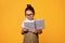 Smart primary school student girl wearing glasses, reads a book, isolated orange background. World Books Day concept