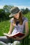 Smart Teenage Girl Sitting In The Grass With Legs Crossed Reading A Book Outdoors