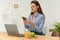 A smart woman remote worker sits at the kitchen table, looking for files on her phone and sending them to her laptop via