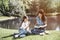 Smart woman is sitting at the edge of small lake with her daughter and reading a book. Her kid is sitting besides her