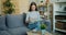 Smart young lady in glasses reading book sitting on comfortable sofa in flat