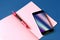 Smartphone with abstract holographic flow on display and pink notebook on classic blue background
