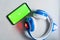 Smartphone with blank green screen mockup with kids wireless headphones  on gray background