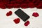 Smartphone rests on a white wooden table on the background of petals and a bouquet of roses