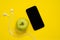 Smartphone and wired headset with green ripe apple on yellow background, top view, copy space for advertising banner of modern