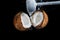 Smash coconut on a black background with an iron hammer blow, spray of coconut milk