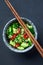 Smashed cucumbers with sesame and chili peppers in a grey bowl on a table with chopsticks. 45 angle view