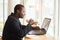 Smile african businessman  sitting in cafe holding a cup of coffee and using laptop