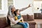 Smile. Joyful happy grandmother smiling while taking selfie with her adorable little granddaughter, sitting on a couch