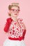Smiled vivacious blond female pointing at the camera in red gloves and glasses on rose pink background