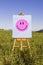 Smiley Face painting on easel in green field. Happiness, creativity, good mood, mental health concepts