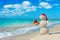 Smiley sandy snowman at beach in christmas hat with golden gift.