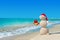 Smiley sandy snowman at beach in christmas hat with golden gift.