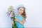 A smiling 5-6-year-old girl in a blue dress and hat on a white isolated background holds a bouquet of flowers, space for text