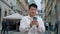 Smiling adult chinese male tourist standing in city holding phone browsing social network using geolocation man traveler