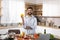 Smiling adult european bearded male hold pepper, prepares salad in modern kitchen interior with organic vegetables