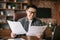 Smiling adult korean male in glasses works with papers, charts and graphs at table in office interior