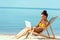 smiling african american female freelancer sitting on deck chair and using laptop on sandy