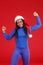 A smiling African-American girl in a blue fitting suit and a Christmas hat, actively dancing with her arms raised.