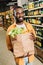 smiling african american male shopper holding paper bag with fruits and vegetables