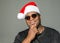 Smiling African American man with hand on his chin wearing a Santa Claus hat against a solid background