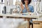 Smiling African-American seamstress shows black thread to camera sitting at workplace with sewing machine