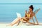 smiling african american woman gesturing by fingers and communicating by laptop while sitting on deck chair on sandy