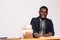 Smiling African businessman at work with large stacks of money on his desk signing a paycheck