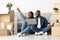 Smiling African Spouses Sitting With Laptop In New Flat And Pointing Away