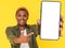 Smiling African student poses with large mobile phone featuring white blank screen, on yellow background with copy space