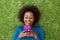 Smiling african woman lying on grass looking at cell phone