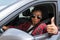 Smiling afro american woman doing a thumbs up gesture in her car: Selective focus. Driving concept.