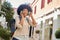 Smiling afro haired woman with headphones walking in city. Portrait of happy latina woman