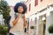 Smiling afro haired woman with headphones walking in city. Portrait of happy latina woman