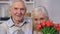 Smiling aged couple embracing, woman smelling flowers, celebrating anniversary