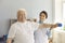 Smiling aged man patient doing physiotherapy exercise with dumbbell under woman chiropractors control