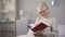 Smiling aged woman in eyeglasses watching photo album, fond memories, family