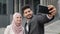 Smiling arabian business colleagues standing on city street and taking selfie on modern smartphone. Woman in hijab