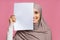 Smiling arabic girl covering half of face with blank paper sheet
