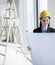 Smiling architect in a hardhat examining a blueprint in an office building