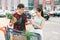 Smiling asian couple standing near shopping cart,man holds pineapple and cheerful woman counts the banknotes