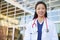 Smiling Asian female healthcare worker outdoors in lab coat